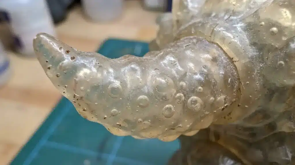 Macro shot of air bubbles and pinholes trapped inside a clear soft vinyl toy horn during the slush casting process.